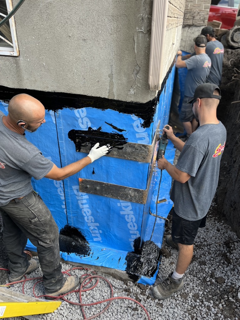 Travailleurs procédant à l'installation d'un drain français autour d'une maison.